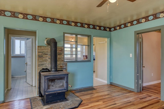 unfurnished living room featuring visible vents, baseboards, ceiling fan, a wood stove, and light wood-style floors