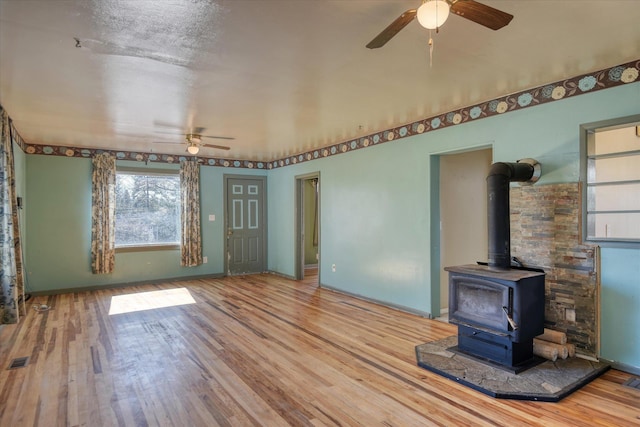 unfurnished living room with visible vents, wood finished floors, a wood stove, and a ceiling fan