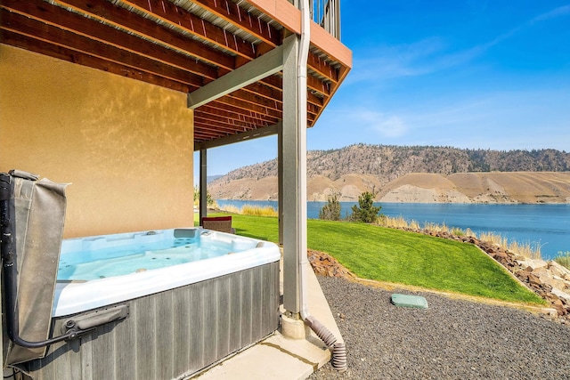 view of patio with a water and mountain view and a hot tub