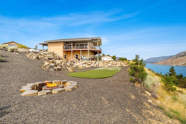 rear view of property with a balcony, a water and mountain view, and an outdoor fire pit