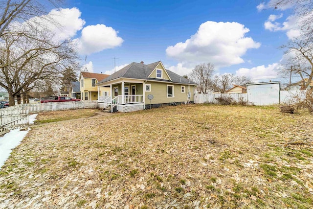 rear view of house featuring a lawn, covered porch, and fence