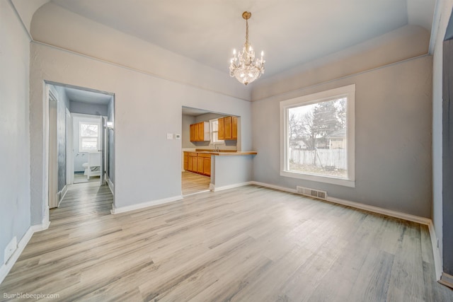 unfurnished dining area featuring visible vents, a notable chandelier, light wood-style flooring, a sink, and baseboards