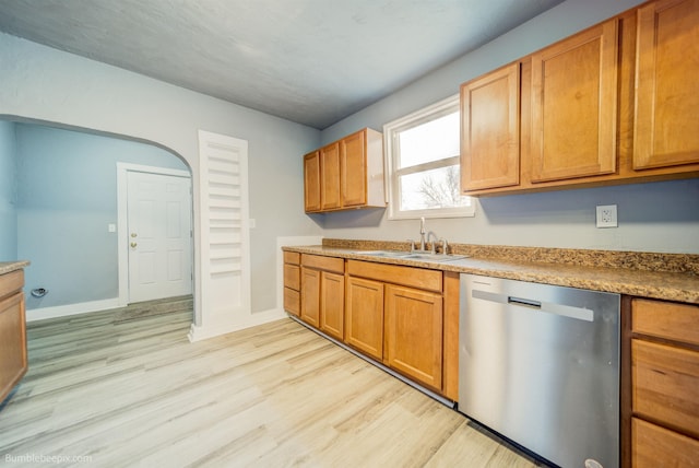 kitchen featuring baseboards, dishwasher, brown cabinets, light wood-style floors, and a sink