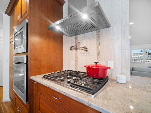 kitchen featuring stainless steel appliances, wall chimney exhaust hood, light stone counters, and dark hardwood / wood-style flooring