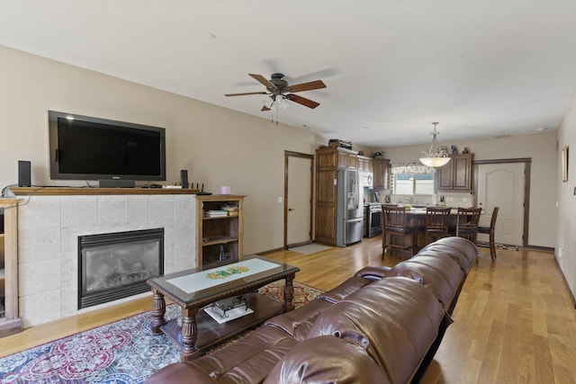 living room with ceiling fan, a tiled fireplace, and light hardwood / wood-style flooring