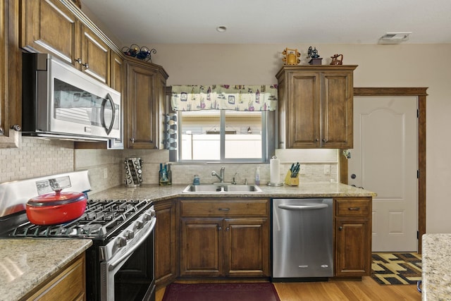 kitchen with light wood-type flooring, light stone countertops, stainless steel appliances, sink, and tasteful backsplash