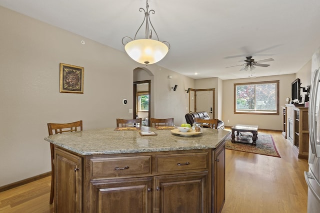 kitchen with light wood-type flooring, ceiling fan, a center island, and plenty of natural light