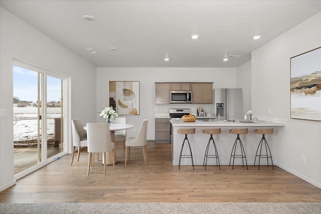 kitchen with appliances with stainless steel finishes, light hardwood / wood-style flooring, a kitchen bar, and kitchen peninsula