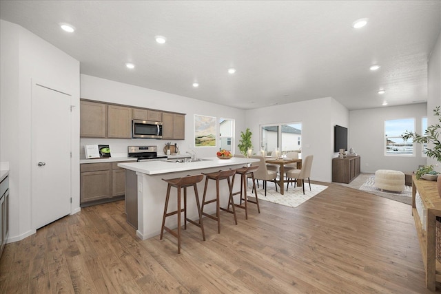 kitchen featuring a kitchen island with sink, appliances with stainless steel finishes, a breakfast bar area, wood-type flooring, and sink