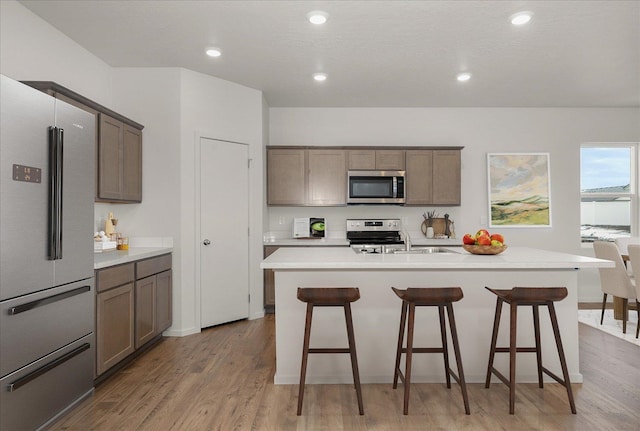 kitchen with a center island with sink, appliances with stainless steel finishes, light hardwood / wood-style flooring, and a kitchen bar