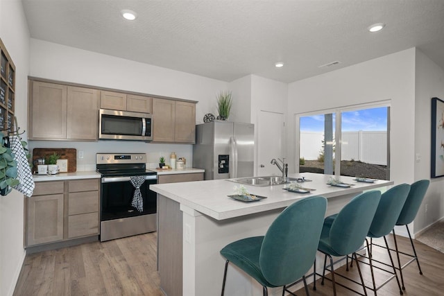 kitchen with stainless steel appliances, a kitchen island with sink, a kitchen breakfast bar, sink, and light hardwood / wood-style floors