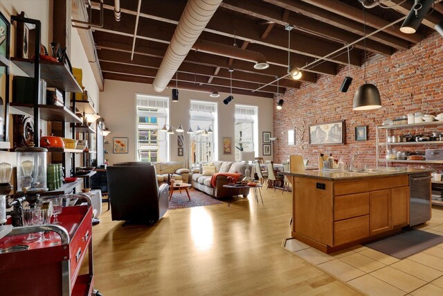 kitchen featuring track lighting, light hardwood / wood-style floors, stainless steel dishwasher, a high ceiling, and brick wall