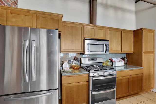 kitchen featuring light stone counters, light tile patterned floors, stainless steel appliances, a high ceiling, and backsplash