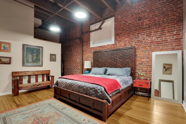 bedroom with a high ceiling, brick wall, and light wood-type flooring