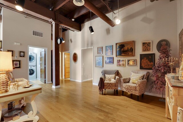 sitting room with high vaulted ceiling, light hardwood / wood-style flooring, beamed ceiling, and stacked washer and clothes dryer