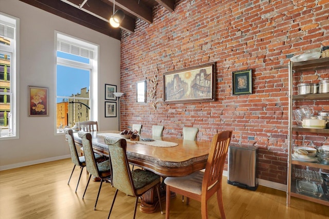 dining room with beamed ceiling, brick wall, and light hardwood / wood-style flooring