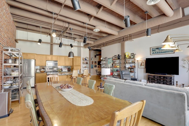 dining area featuring a high ceiling, brick wall, and light wood-type flooring