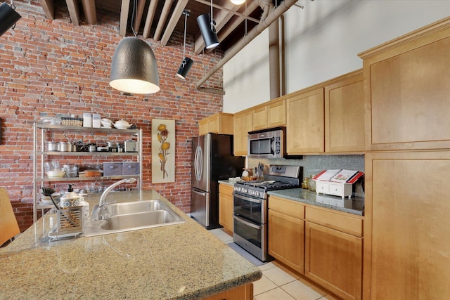 kitchen with light tile patterned flooring, sink, appliances with stainless steel finishes, a towering ceiling, and brick wall