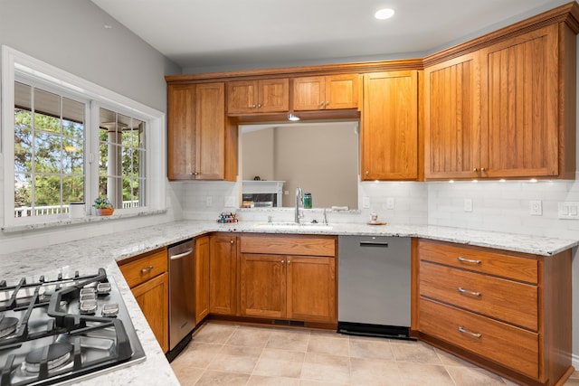 kitchen with brown cabinets, a sink, gas stovetop, and light stone countertops