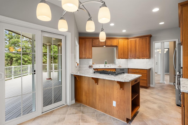 kitchen featuring brown cabinetry, hanging light fixtures, a peninsula, and light stone countertops