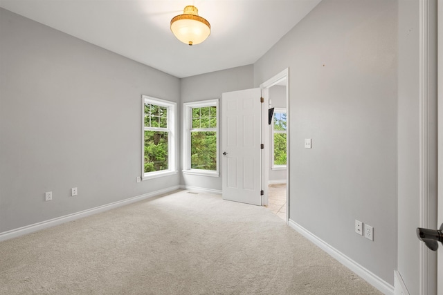 spare room with baseboards and light colored carpet