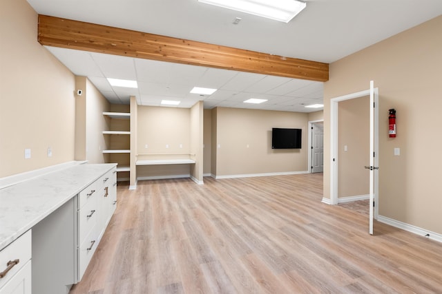 interior space with baseboards, a drop ceiling, and light wood finished floors