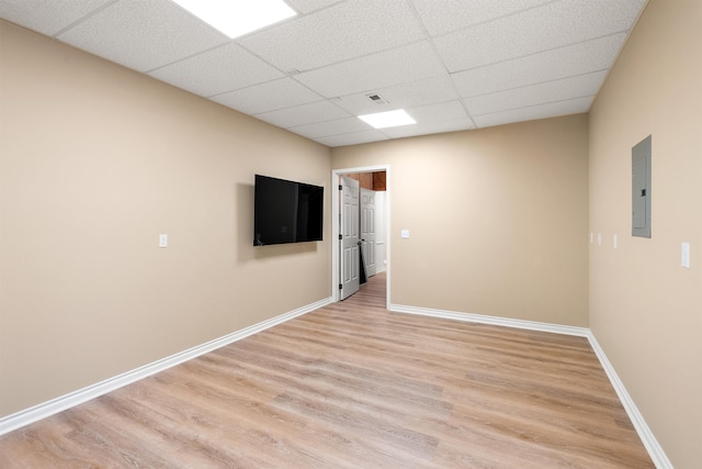 unfurnished room with a paneled ceiling, electric panel, baseboards, and wood finished floors