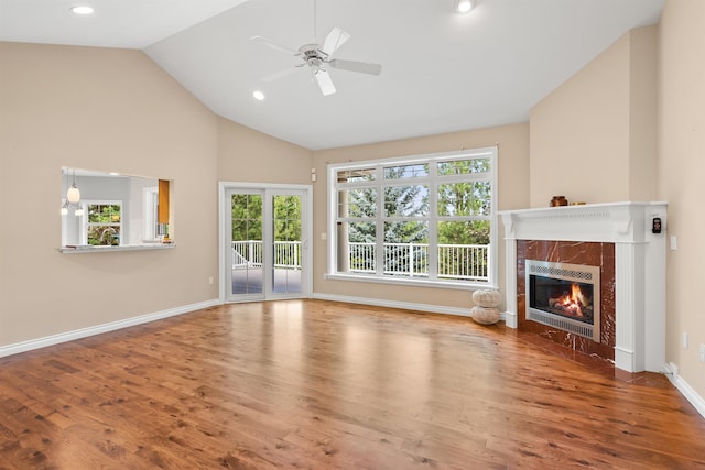 unfurnished living room with a ceiling fan, vaulted ceiling, a tiled fireplace, and wood finished floors