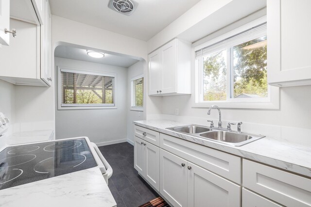 kitchen with white cabinets, stove, light stone counters, and sink