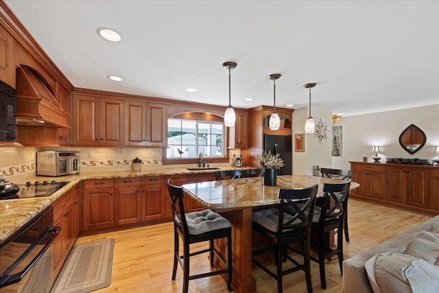 kitchen with black appliances, custom exhaust hood, decorative light fixtures, and light stone countertops