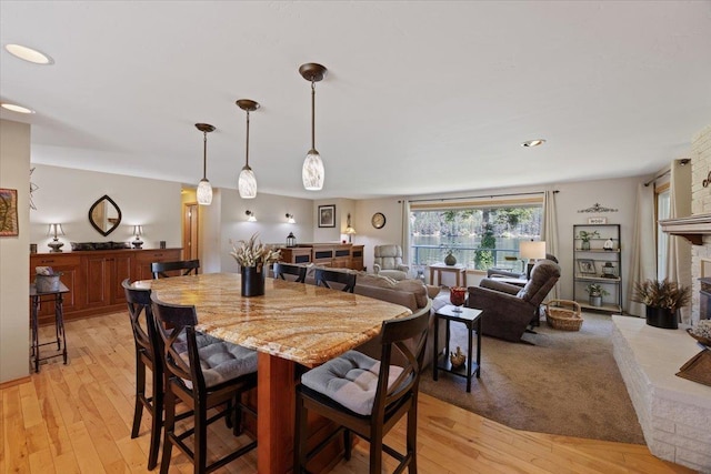 dining area featuring light wood-type flooring and a fireplace with raised hearth