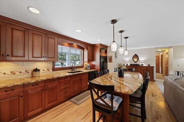 kitchen featuring a sink, black fridge with ice dispenser, open floor plan, hanging light fixtures, and backsplash