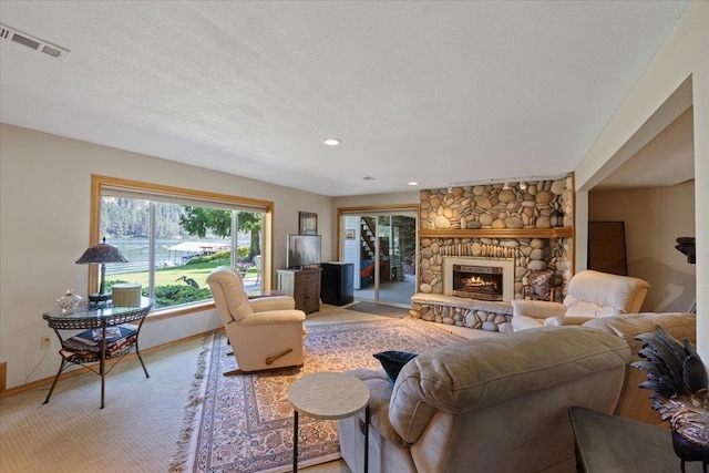 living area with light carpet, baseboards, visible vents, a textured ceiling, and a stone fireplace