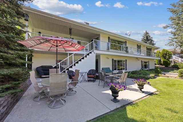 rear view of house featuring a lawn, a balcony, stairway, a patio area, and outdoor dining space