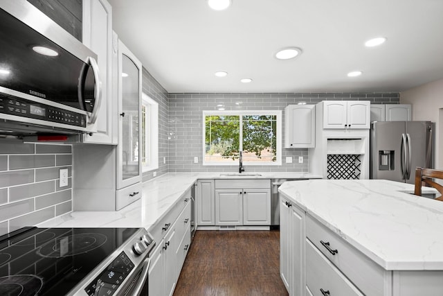 kitchen with stainless steel appliances, decorative backsplash, sink, light stone countertops, and dark hardwood / wood-style flooring