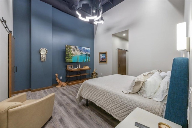 bedroom with a high ceiling, a barn door, wood-type flooring, and a notable chandelier