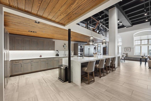 kitchen featuring sink, stainless steel double oven, a kitchen breakfast bar, light stone countertops, and wood ceiling