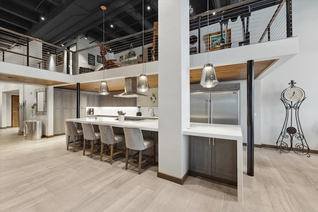 kitchen with wall chimney range hood, light wood-type flooring, a high ceiling, built in fridge, and decorative light fixtures