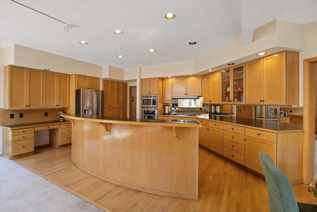 kitchen featuring light wood-type flooring, appliances with stainless steel finishes, glass insert cabinets, and a breakfast bar area