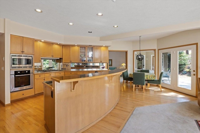 kitchen featuring a breakfast bar, light wood finished floors, stainless steel appliances, recessed lighting, and glass insert cabinets