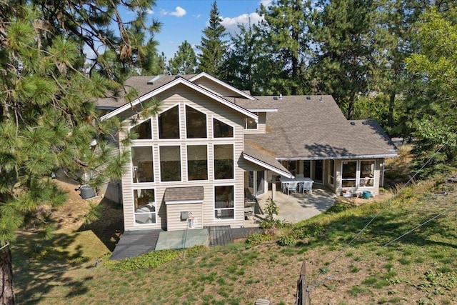 rear view of property featuring a shingled roof, a lawn, and a patio area