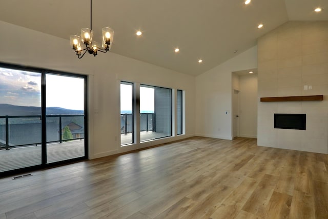 unfurnished living room with a mountain view, a tile fireplace, high vaulted ceiling, light hardwood / wood-style floors, and an inviting chandelier