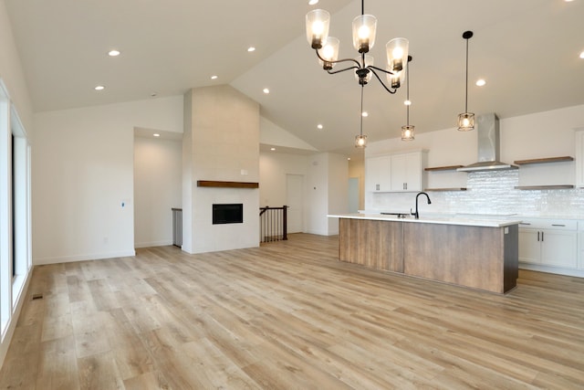 kitchen with light hardwood / wood-style flooring, backsplash, wall chimney exhaust hood, a kitchen island with sink, and white cabinetry