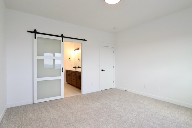 unfurnished bedroom with light colored carpet, ensuite bathroom, and a barn door