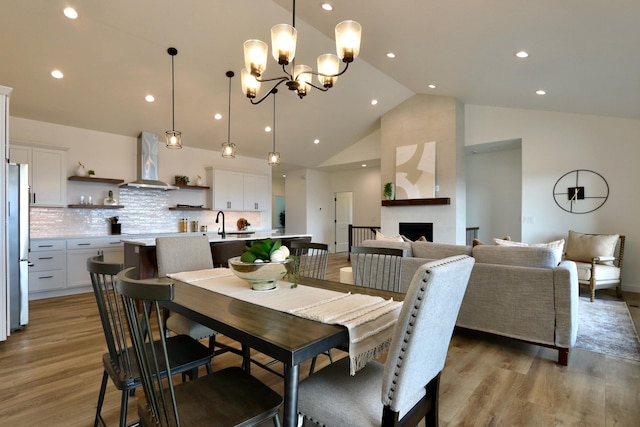 dining area featuring high vaulted ceiling, light hardwood / wood-style floors, sink, a fireplace, and an inviting chandelier