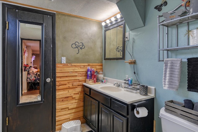 bathroom featuring wood walls, vanity, tile patterned flooring, a textured ceiling, and toilet