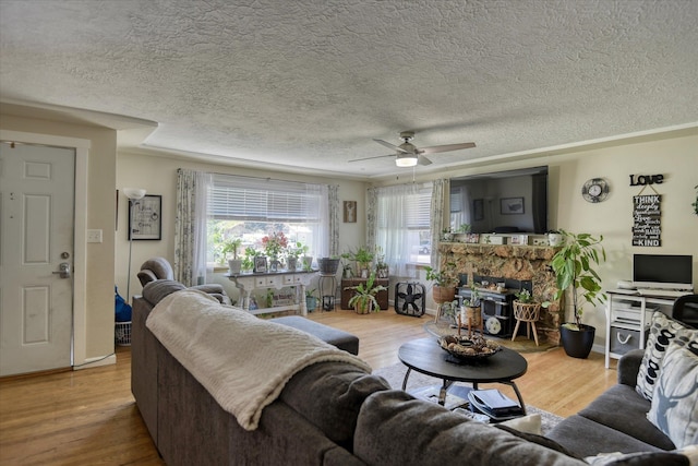 living room with a fireplace, light hardwood / wood-style flooring, ceiling fan, and a textured ceiling