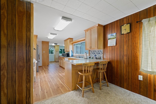 kitchen featuring a breakfast bar, wooden walls, kitchen peninsula, and light carpet