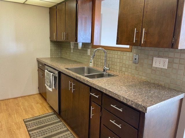 kitchen with light hardwood / wood-style floors, stainless steel dishwasher, dark brown cabinetry, sink, and tasteful backsplash