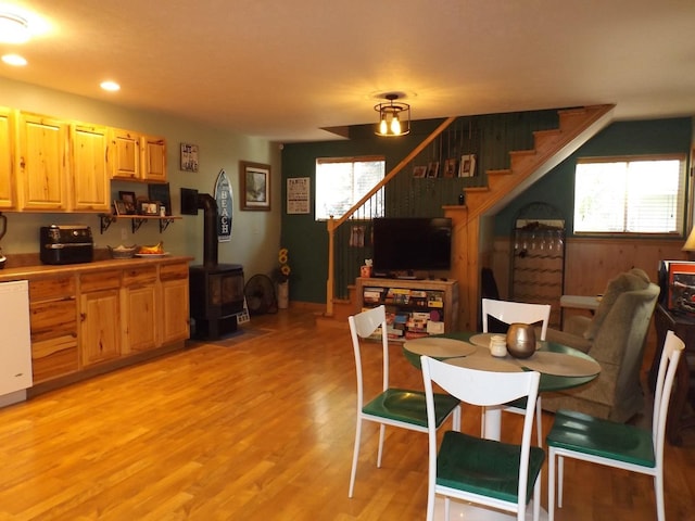 dining area featuring a wood stove, light wood-style flooring, a wealth of natural light, and stairway